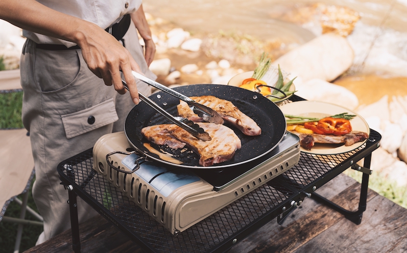 Person bereitet Fleisch auf einen Camping Kocher zu