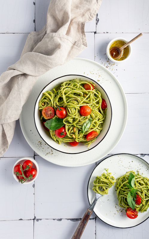 Spaghetti mit grünen Pesto und Tomaten garniert mit Basilikum in einer weißen Schüssel 